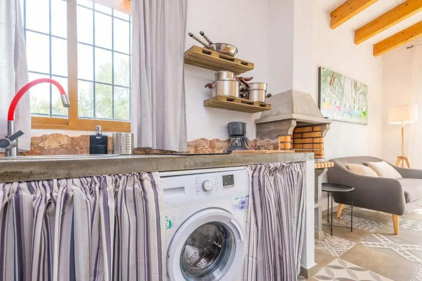 A kitchen and living area with a washing machine beneath the counter and a fireplace nearby.
