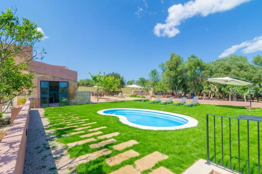 An outdoor swimming pool sits in a landscaped garden with lawn and lounge seating.