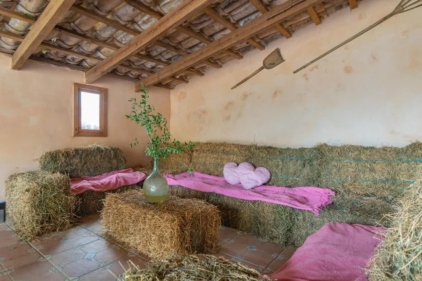 A rustic room with hay bales arranged around pink fabric and a potted plant.