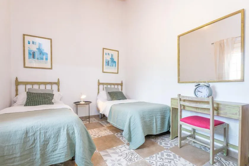 A bedroom with two beds and a desk beneath a wall mirror.