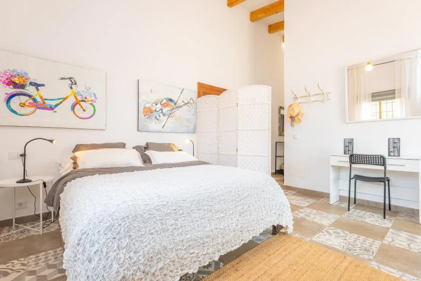A bright bedroom with a large bed, colorful wall art, and a desk.