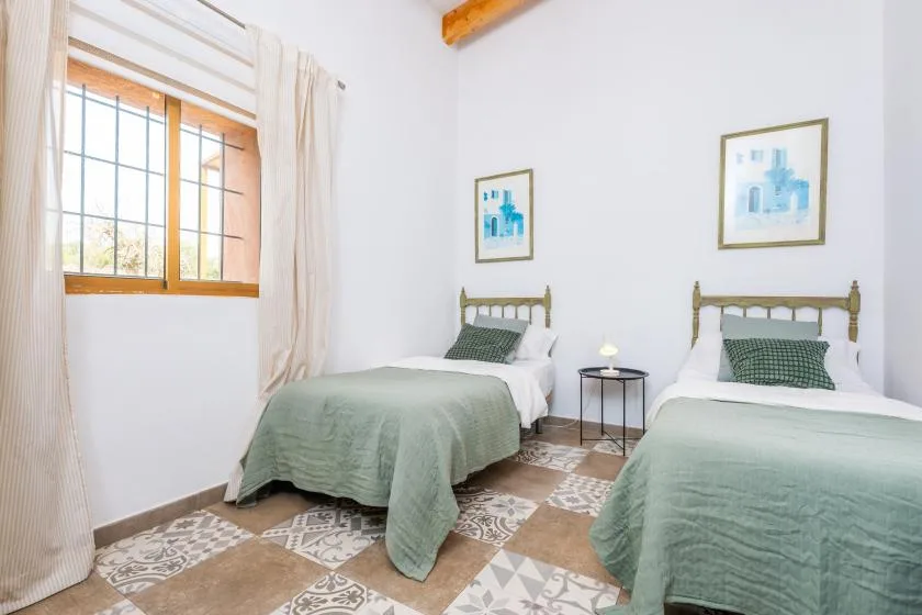 A twin bedroom with two beds, green bedding, and a window.