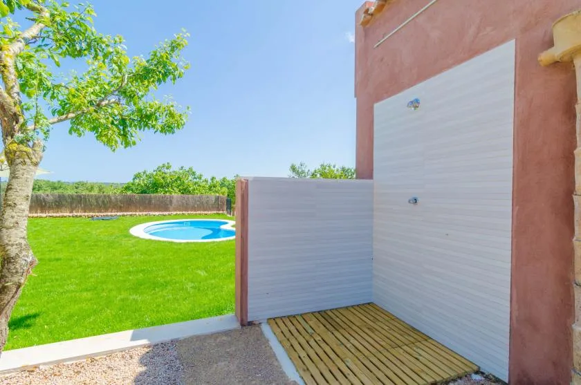 An outdoor shower area opens onto a green lawn with a small pool.