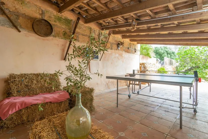 A covered patio has a table tennis table and a hay bale seating area.