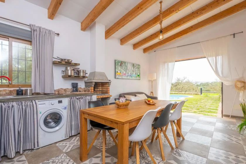 A bright kitchen and dining area with a wooden table beside a large open doorway.