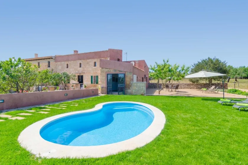 A curved swimming pool sits in a green lawn beside a low-rise building.