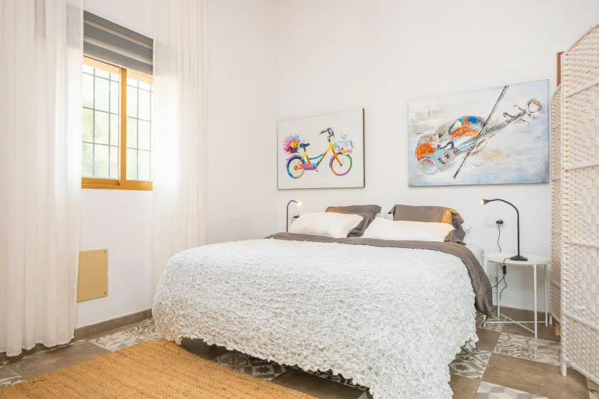 A bright bedroom with a neatly made bed and colorful wall art.