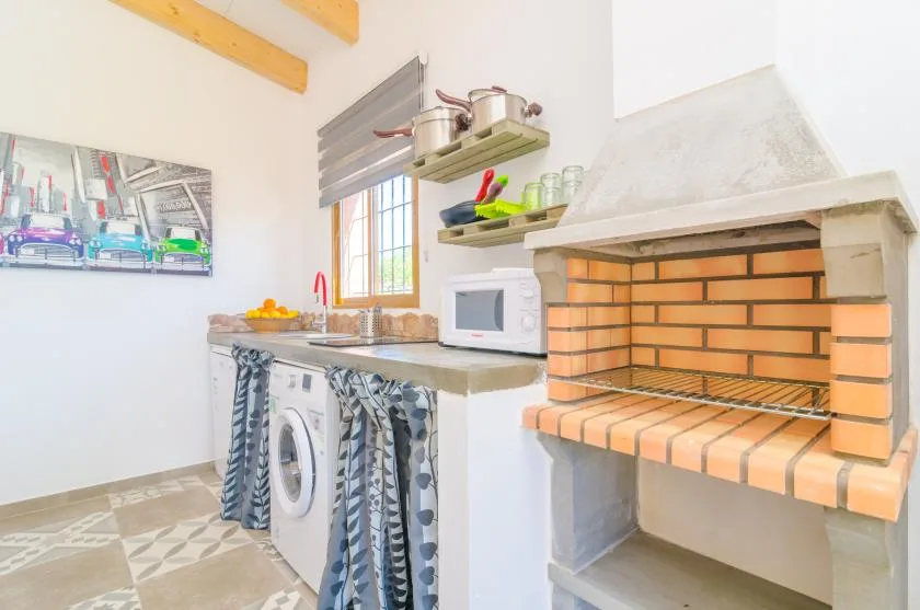 A bright kitchen with a brick barbecue, microwave, and washing machine.