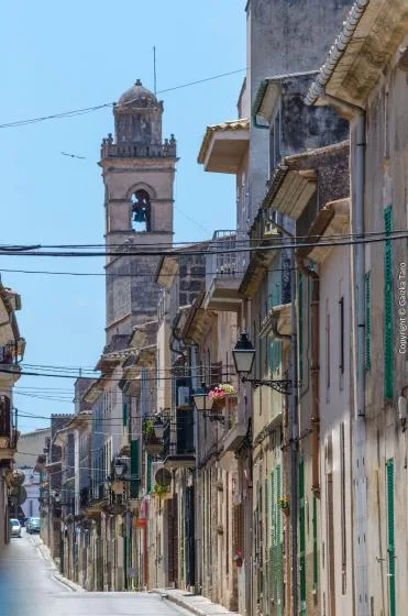 A narrow street lined with old buildings leads toward a stone bell tower.