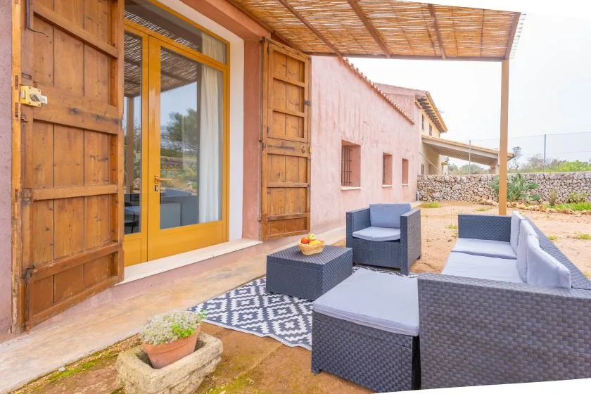 A covered patio has woven seating beside a wooden door.