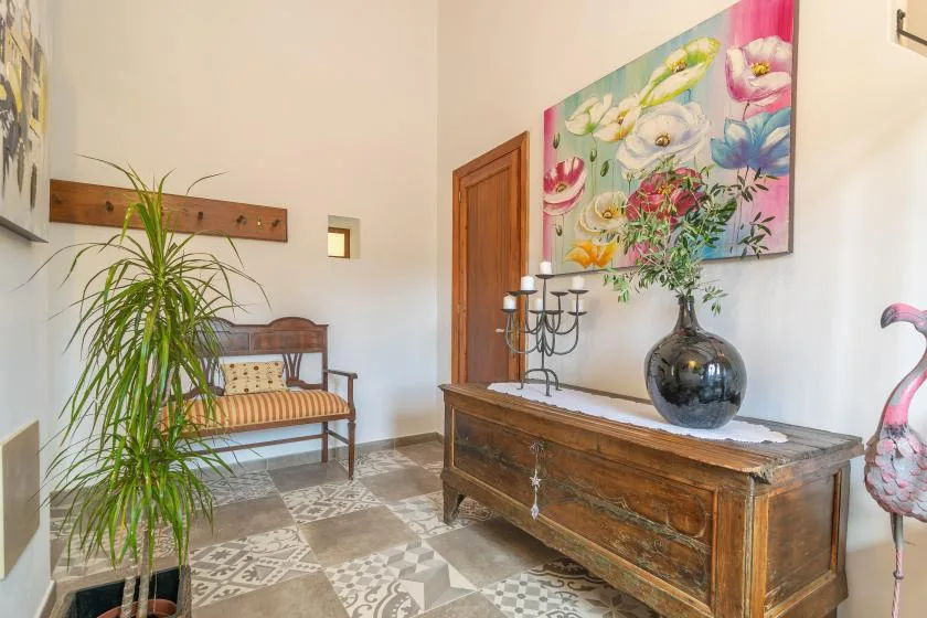 A bright entryway features a wooden bench, a console table, and colorful floral artwork.