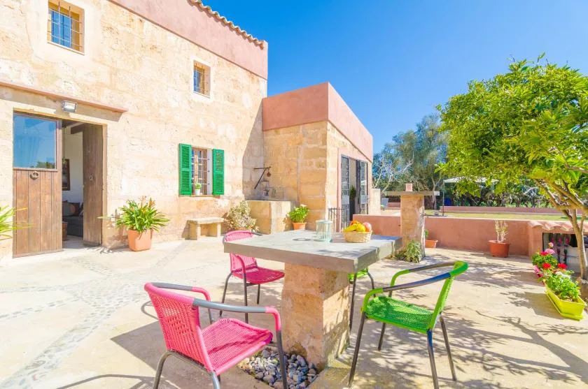 A sunny stone terrace with a table, colorful chairs, and potted plants.