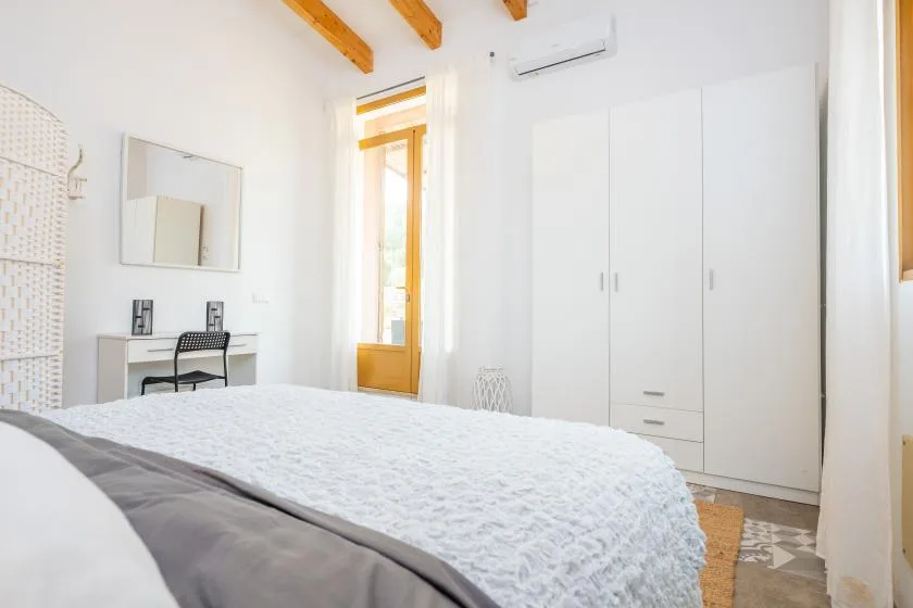 A bright bedroom with a bed, a desk, and a large wardrobe.