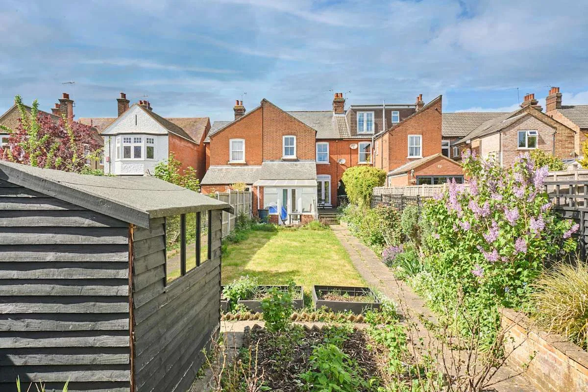 A garden with a lawn, planted beds, and a dark wooden shed.