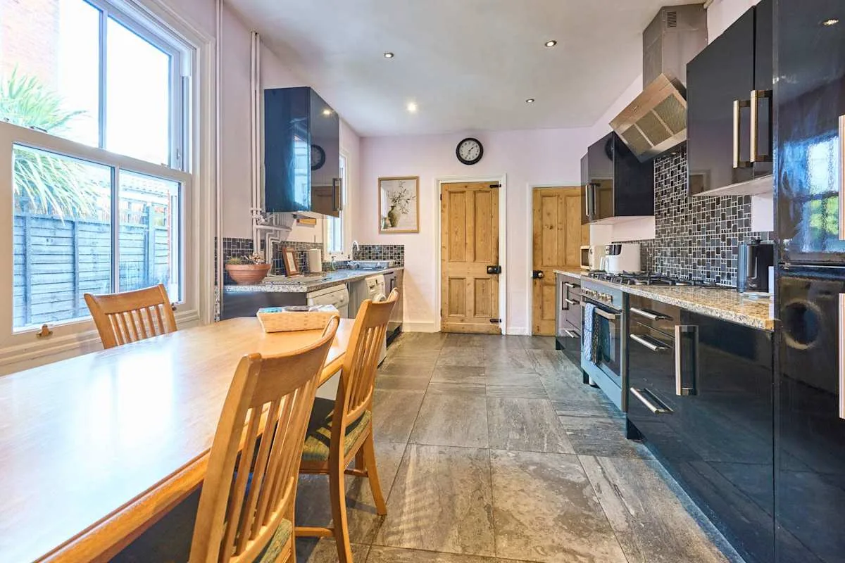 A kitchen with a long dining table and dark cabinets.
