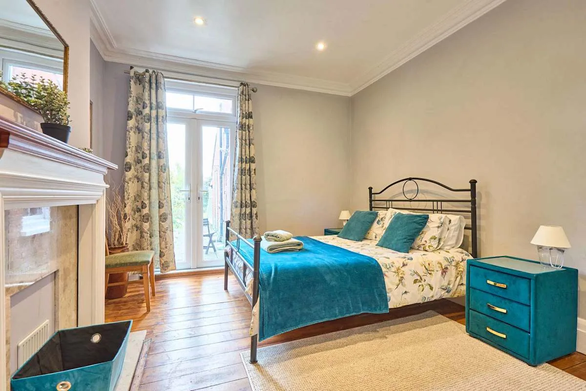 A bedroom with a bed dressed in teal bedding beside a window.