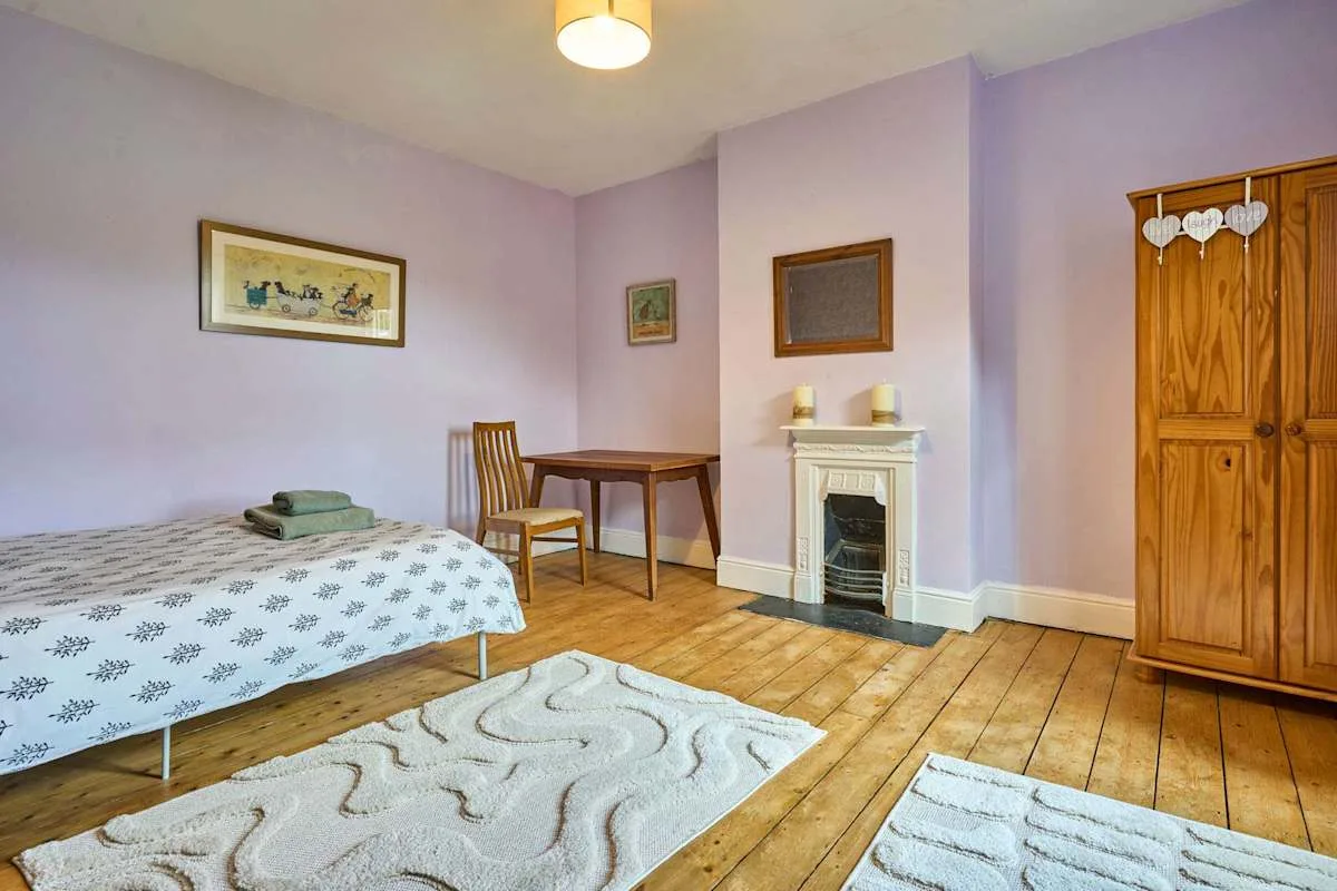 A bedroom with a bed, wooden floor, and fireplace.