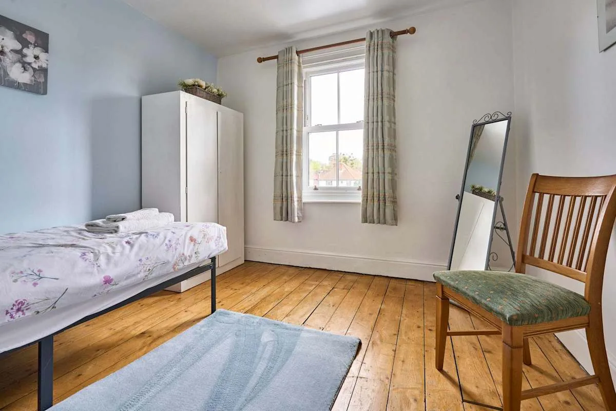 A bedroom with a single bed, a window, and a wooden chair.