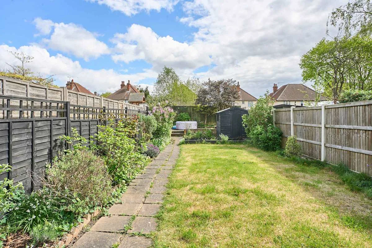 A fenced garden with a paved path, lawn, and small shed.