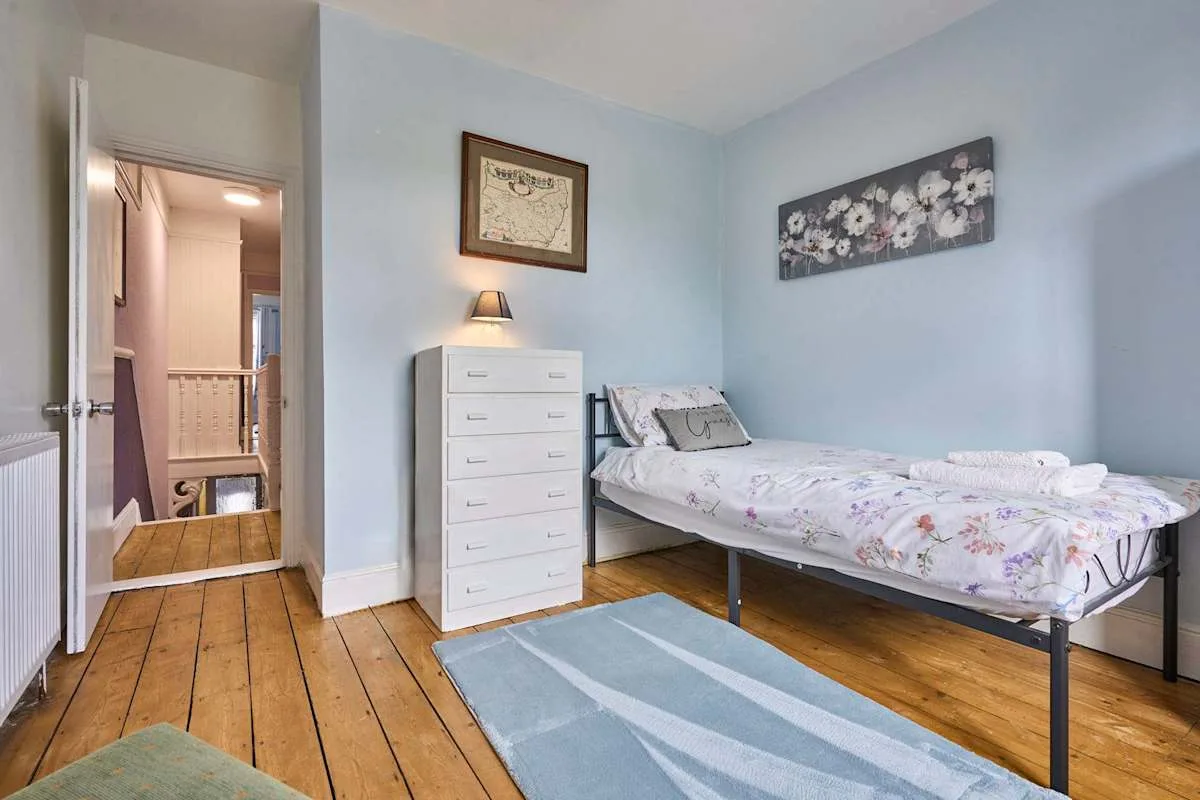 A bedroom with a single bed, a white dresser, and a blue rug.