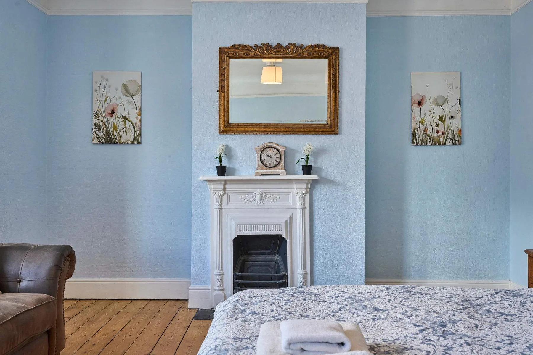 A bedroom with a bed, fireplace, and mirror against a pale blue wall.