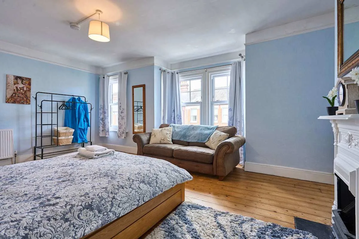 A bedroom with a bed, a sofa, and tall windows.