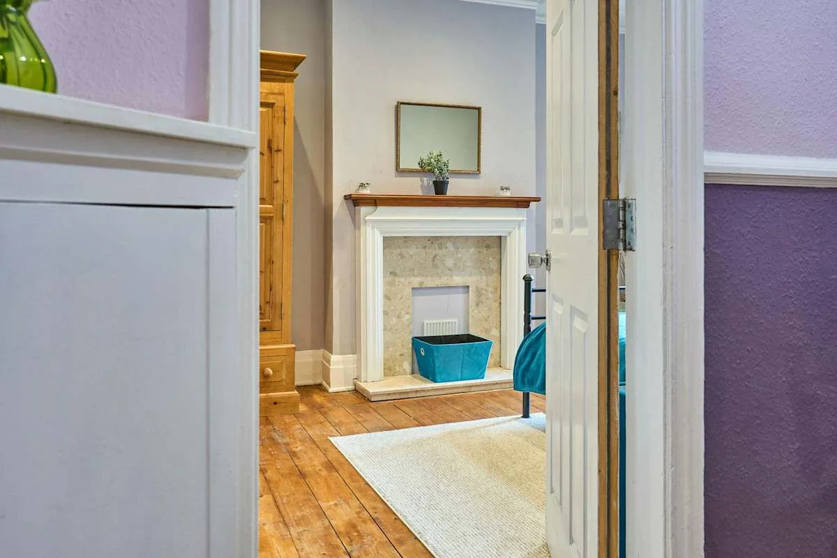 A bright sitting room with a fireplace, wooden flooring, and a pale rug.