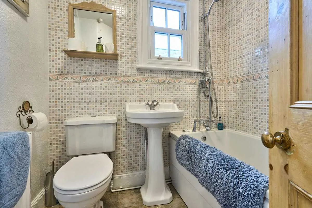 A tiled bathroom with a pedestal sink, toilet, and bathtub.