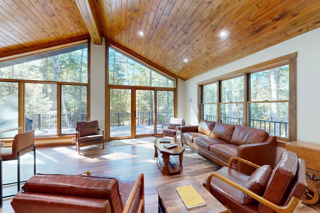 Una sala de estar luminosa con asientos de cuero y grandes ventanas con vista a los árboles.