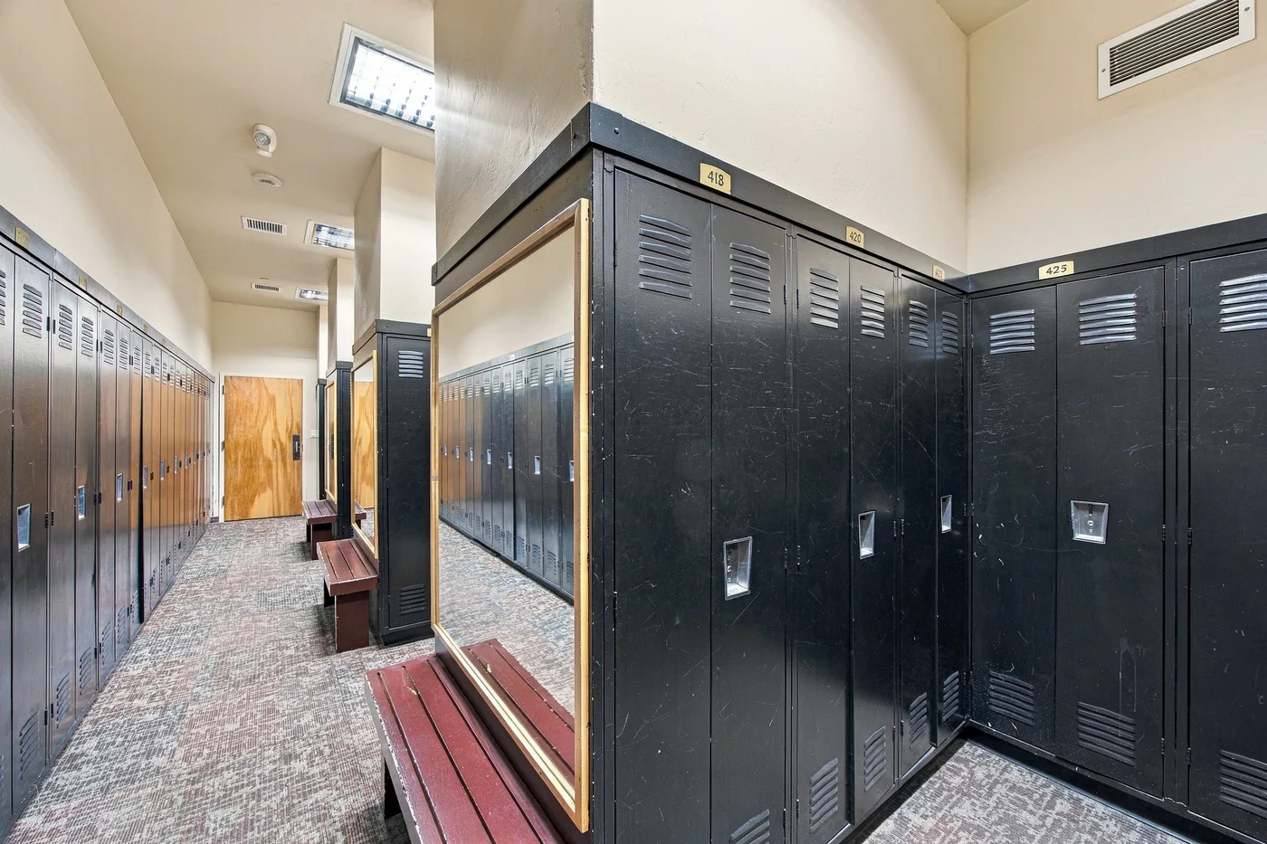 A locker room with rows of lockers and benches along a carpeted aisle.