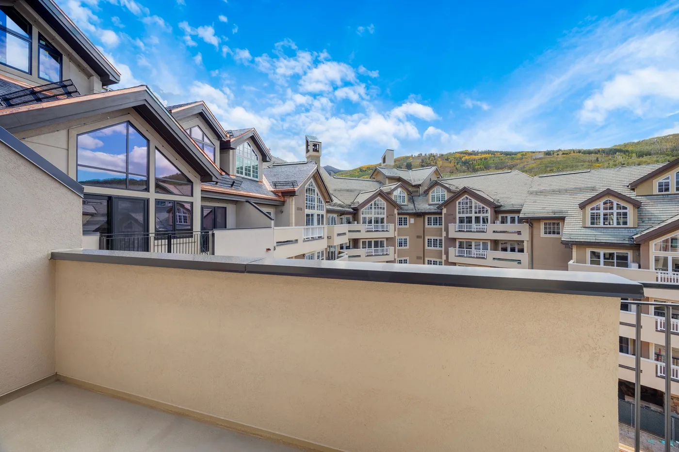 Balcony overlooking neighboring buildings and a green hillside beneath a blue sky.