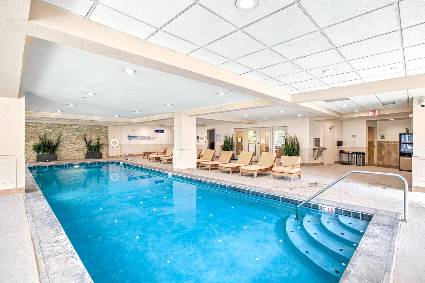 An indoor swimming pool with curved steps and lounge seating along the edge.