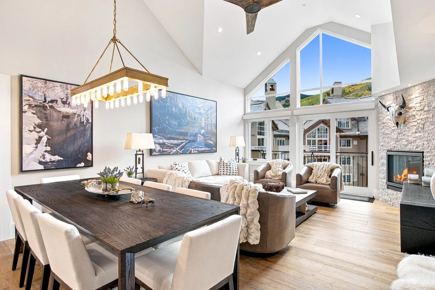 A bright open-plan living and dining room has tall windows and a dining table.