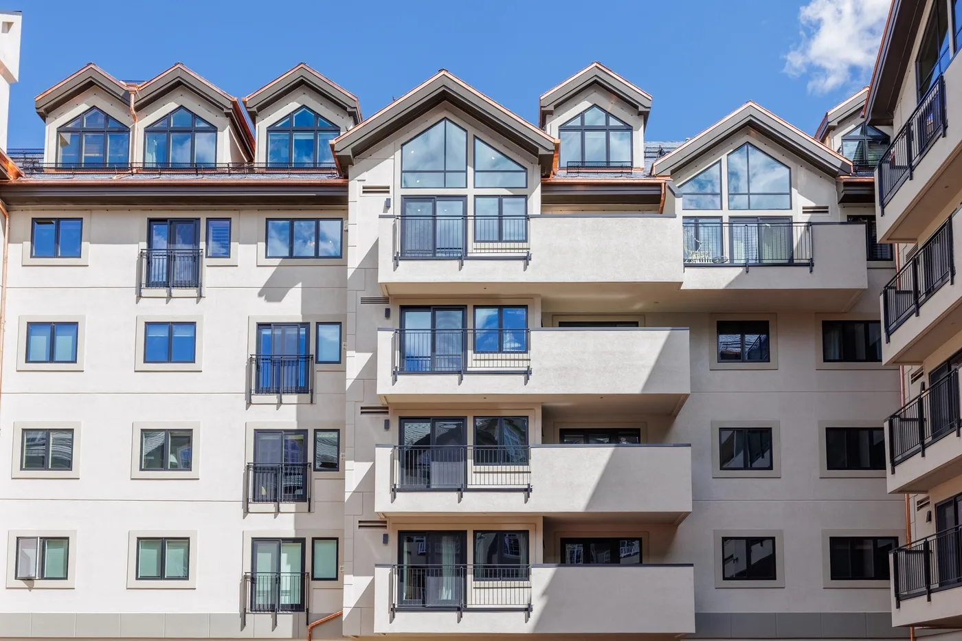 Edificio residencial de varios pisos con balcones y muchas ventanas bajo un cielo azul.