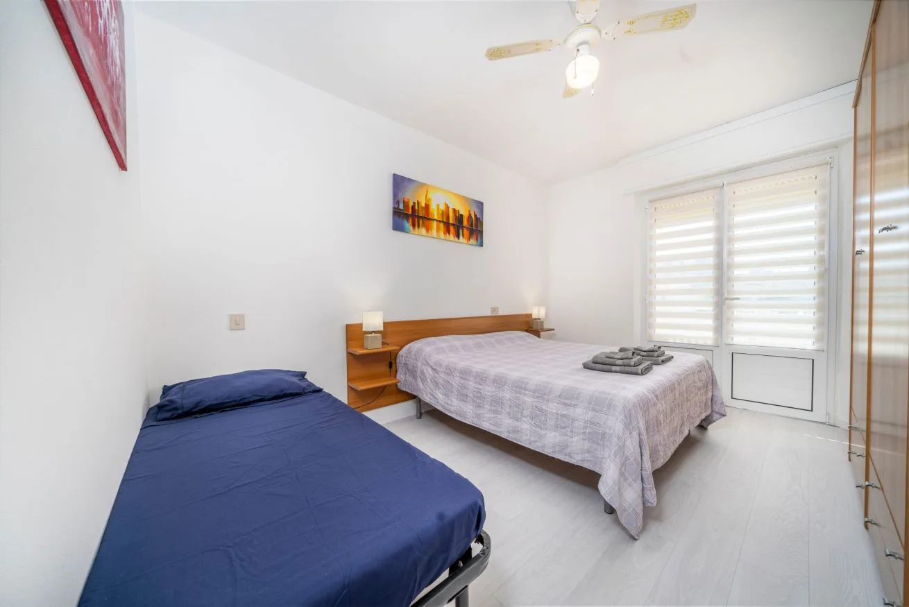 A bedroom with two beds and a window with blinds.