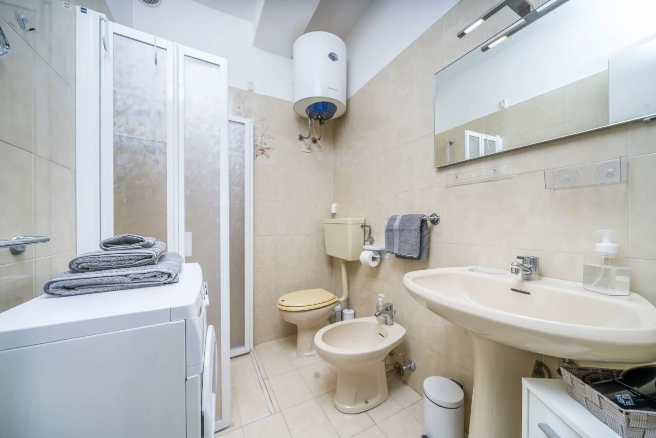A tiled bathroom with a sink, toilet, bidet, and washing machine.