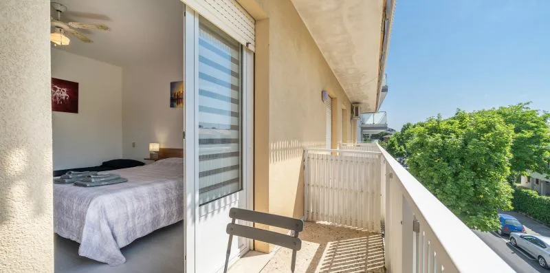 A bedroom opens onto a balcony with a white railing and leafy treetops beyond.