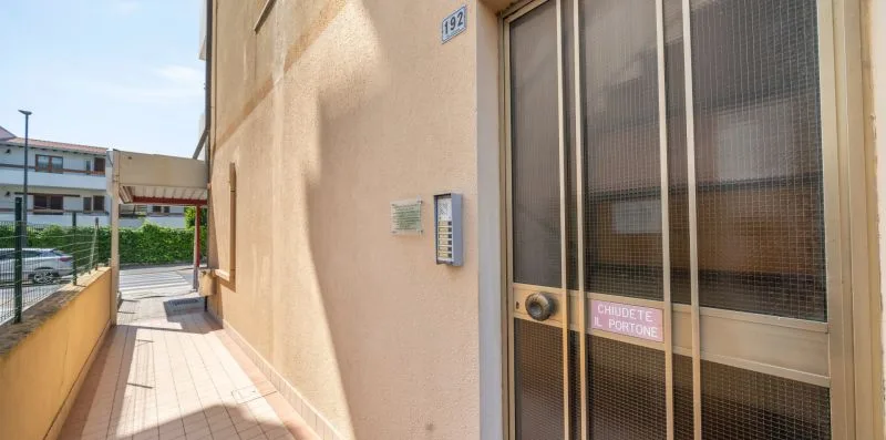 A narrow outdoor walkway runs beside a building entrance with a screened door.