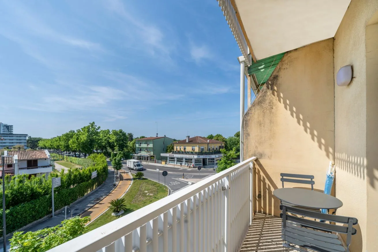 A balcony with seating overlooks a leafy neighborhood street.