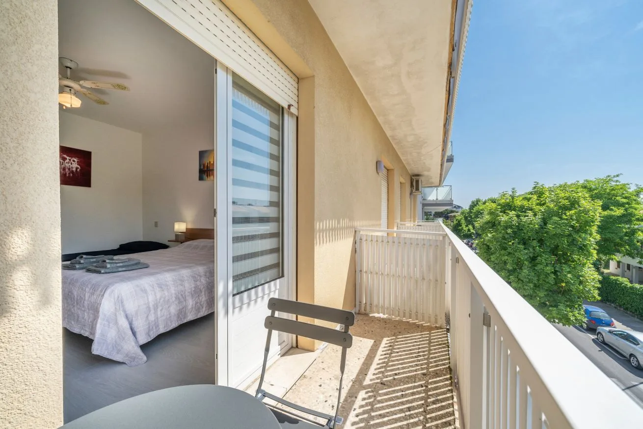 A bedroom opens onto a narrow balcony with a white railing.