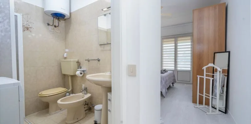 A bathroom with a toilet, bidet, and sink opens onto a bedroom.