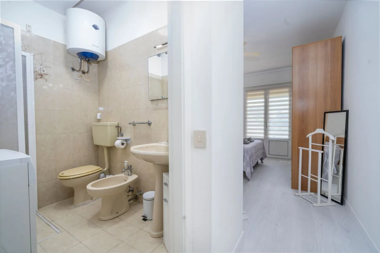 A bathroom with a toilet, bidet, and sink opens onto a bedroom.