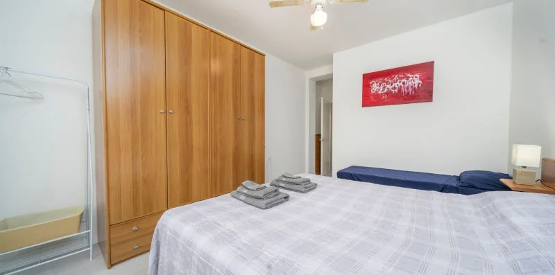 A bedroom with a bed, wooden wardrobe, and red wall art.