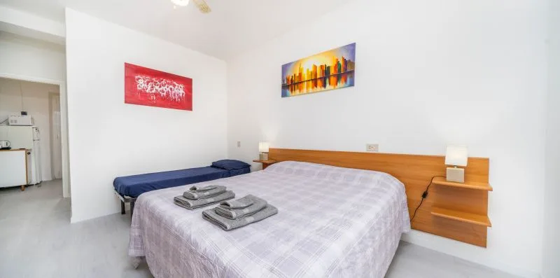A bedroom with a neatly made bed, folded towels, and colorful wall art.