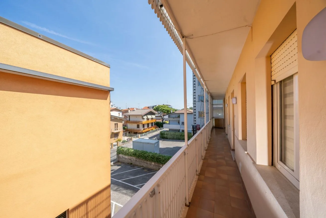 A covered exterior corridor overlooks nearby residential buildings and a parking area.