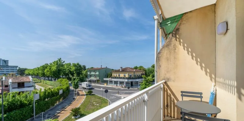 A balcony overlooks a tree-lined street and nearby buildings.