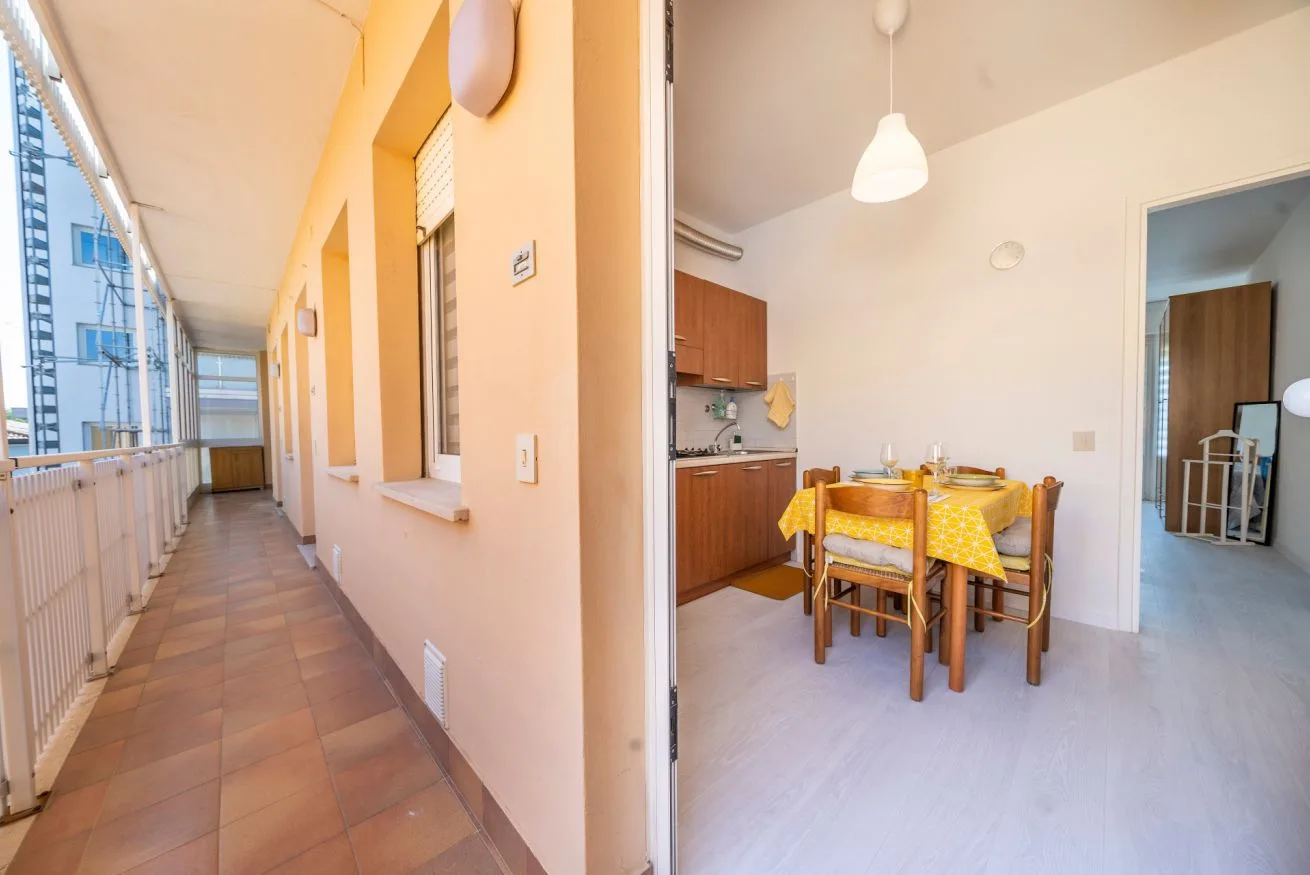 A dining area with a yellow tablecloth sits beside a long enclosed balcony.
