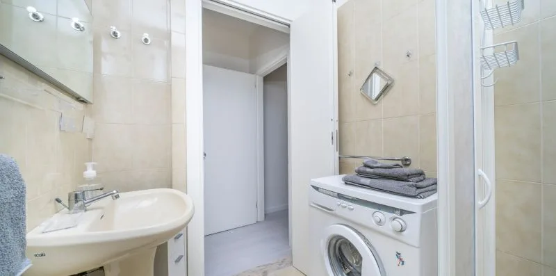 A tiled bathroom with a sink and a washing machine beside an open doorway.