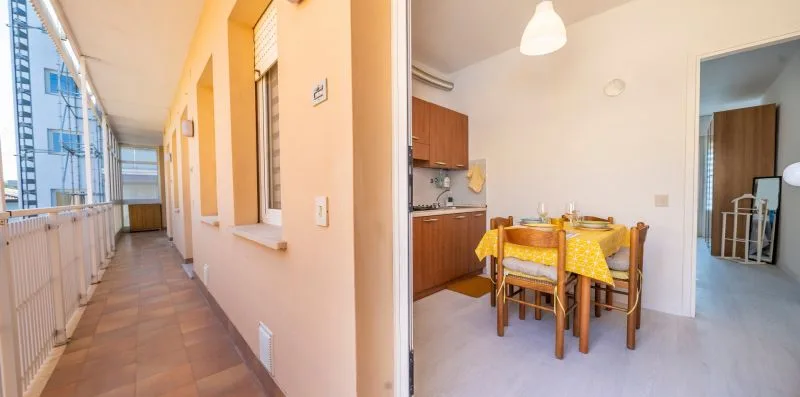 A dining area with a yellow tablecloth sits beside a kitchen and open balcony corridor.