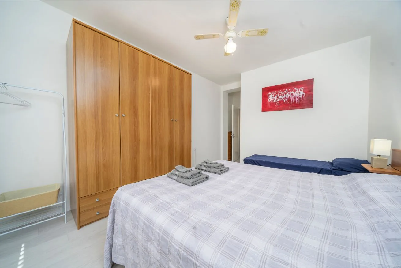 A bedroom with a large bed, wooden wardrobes, and a ceiling fan.